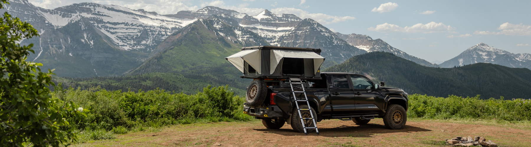 Rooftop tent mounted on black truck parked at scenic mountain overlook with ladder deployed