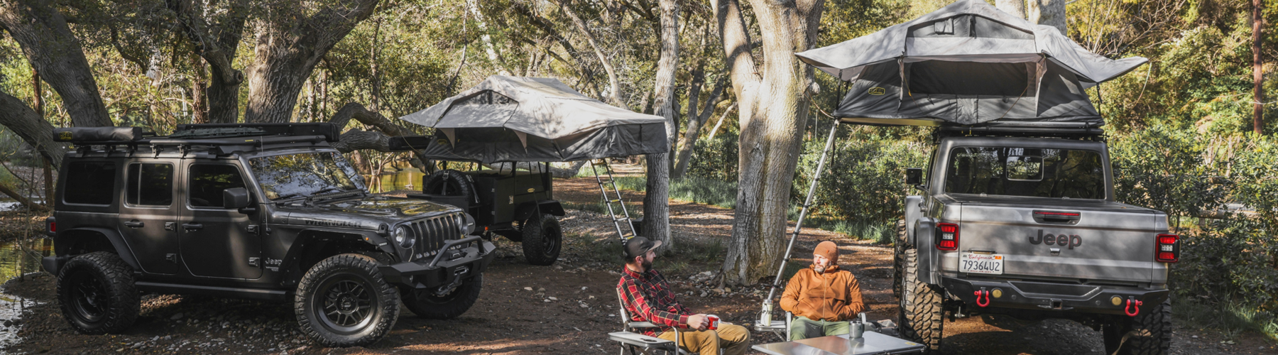 Overlanding campsite with two Jeep vehicles featuring rooftop tents set up in wooded area